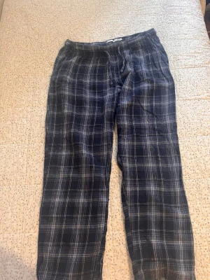 Mörkblå rutiga pyjamasbyxor - Mysiga pyjamasbyxor i mörkblått med vitt rutmönster. Byxorna har resår i midjan och är tillverkade i mjukt tyg, perfekt för slappa dagar hemma. Klassisk och avslappnad stil som passar alla som gillar bekväma sovkläder.