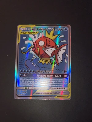 Pokémonkort Magikarp & Wailord GX - Säljer ett Pokémonkort med Magikarp & Wailord GX TAG TEAM. Kortet har en färgstark och glansig design med Magikarp i rött och vitt samt Wailord i blått. Kortet har HP 300 och attacker som Super Splash och Towering Splash GX. Perfekt för samlare eller Pokémonfans.