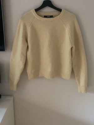 Gul stickad tröja med rund hals - Mysig stickad tröja med rund halsringning och långa ärmar. Tröjan har ribbstickade muddar vid ärmslut och nederkant. Perfekt för lager på lager och enkel att matcha med olika outfits.