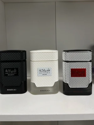 Khadlaj- snow, Shadow och shiyaaka bundle  - Säljer tre olika Shiyaaka parfymer från Khadlaj. Flaskorna har en modern, fyrkantig design med texturerad yta. En är helsvart, en vit och en silverfärgad med röd etikett. Alla flaskor har eleganta detaljer och ser riktigt lyxiga ut.