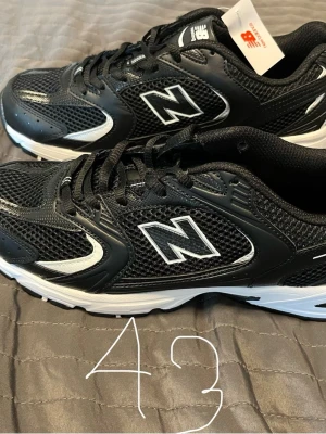 Svarta New Balance sneakers strl 43 - Snygga svarta sneakers från New Balance med vita detaljer och meshpaneler för extra ventilation. Klassisk låg modell med bekväm sula och tydlig N-logga på sidan. Perfekta för dig som gillar sportig och stilren look.