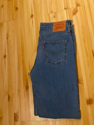 Ljusblå raka jeans från Levi's - Säljer ett par klassiska ljusblå jeans från Levi's med rak passform och hög midja. Jeansen har fem fickor, gylf med knappstängning och Levi's ikoniska läderpatch bak i midjan. Perfekta till en avslappnad stil och tillverkade i slitstark denim. 