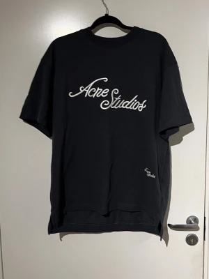 Svart Acne Studios t-shirt - Säljer en svart t-shirt från Acne Studios med vit broderad logga på bröstet. T-shirten har en klassisk passform med rund hals och korta ärmar. Perfekt för dig som gillar stilrena och trendiga plagg.