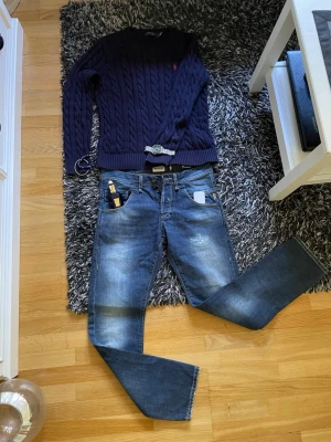 Blå raka jeans från Riorim - Säljer ett par blå jeans från Riorim med raka ben och klassisk femficksdesign. Jeansen har snygga slitningar och tvättade detaljer som ger en cool, avslappnad look. Perfekta för dig som gillar en casual stil och vill ha ett par jeans som funkar till det mesta. Priset är ej hugget i sten så kom gärna med bud!