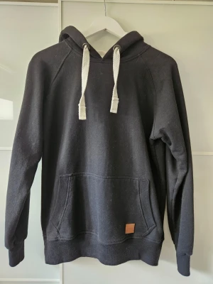 Svart hoodie från Amaci & Sons - Säljer en svart hoodie från Amaci & Sons med vit insida i huvan och vita, breda dragsnören. Storlek M