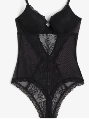 Svart spetsbody  - Snygg svart body i genomskinlig mesh och spets med vadderade kupor och justerbara axelband. Spetsdetaljer framtill och längs kanterna ger en feminin look. Perfekt att styla under en skjorta eller till jeans för en trendig outfit. Från hm. ENDAST ANVÄND EN GÅNG