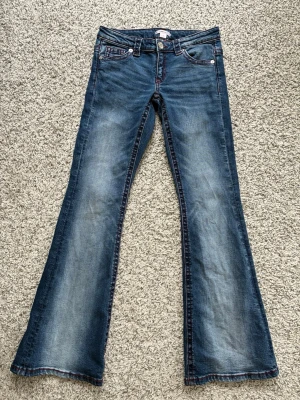 Ginatricot - Blå bootcut jeans med röd söm - Snygga blå bootcut jeans med markerad röd söm och broderade bakfickor. Jeansen har klassisk femficksmodell och lätt slitna detaljer framtill och baktill. 