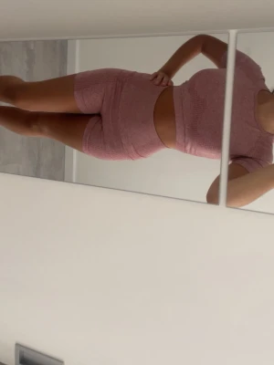 Dimmrosa  set med shorts och topp - Säljer ett rosa sömlöst set med kortärmad crop top och matchande höga shorts. Setet är i stretchigt, ribbat material som sitter tajt och bekvämt. Perfekt för dig som gillar sportig och trendig stil. 