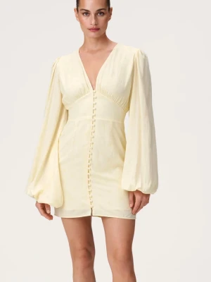 Adoore klänning  - Kort klänning i ljusgul ton med v-ringning och långa puffärmar. Klänningen har dekorativa knappar framtill och markerad midja för en feminin siluett. Tillverkad i ett lätt material som ger ett elegant fall.