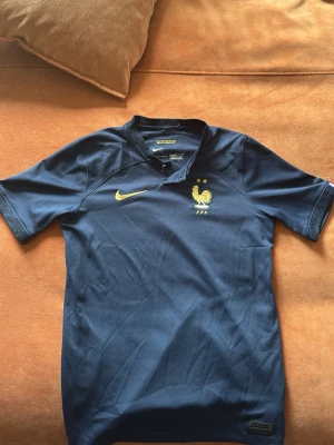  Frankrike fotbollströja från vm 2022  - Säljer en mörkblå fotbollströja från Nike med Frankrikes landslagsemblem och två stjärnor på bröstet. Tröjan har korta ärmar, gul Nike-logga och är tillverkad i ett lätt, ventilerande material som passar perfekt till träning eller match. Köpt från Nikes hemsida 👌