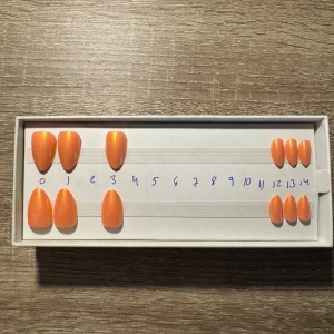 Sunset Spritz press-on naglar - Snygga press-on naglar i modellen Sunset Spritz med kort mandelform. Naglarna har en skimrande orange färg som verkligen poppar. Perfekt för dig som vill ha en trendig och fräsch look utan att behöva gå till salongen. Materialet är tåligt och lätt att applicera. Säljes utan tillbehör och storlekar x2.