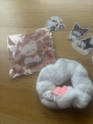 Vit fluffig scrunchie med kattdekor - Supergullig vit scrunchie i mjukt, fluffigt tyg med en söt kattdekor och rosa rosetter. Perfekt för att ge din frisyr en extra söt touch och passar till många olika stilar. Materialet känns mjukt och bekvämt i håret.