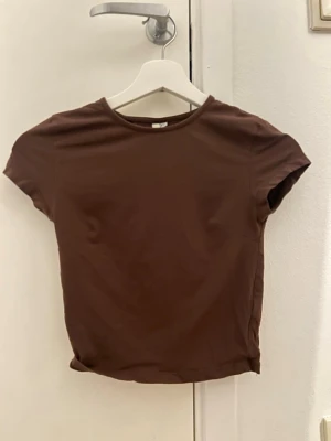 Brun basic t-shirt med kort ärm - En enkel brun t-shirt med rund hals och korta ärmar. Modellen är rak och har en klassisk passform som funkar till det mesta. Tillverkad i mjukt bomullstyg för en bekväm känsla. Perfekt att matcha med jeans eller kjol.
