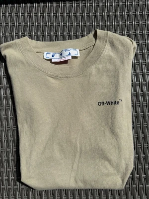 Beige Off-White t-shirt  - Säljer en beige t-shirt från Off-White med logga på framsidan och baksidan. Klassisk rund hals och mjukt bomullsmaterial. Väldigt unik och snygg färg!