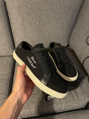  Saint Laurent skor - Svarta sneakers från Saint Laurent med vit sula och handskriven logga på sidan. Skorna har svarta skosnören, detaljer i läder och canvasmaterial. Klassisk låg modell som passar till det mesta och ger en clean look.