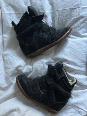 Svarta Isabel Marant skor - Isabel Marant skor i storlek 38. Köpta på Sellpy så har tyvärr inget kvitto/dustbag från Isabel Marant, men har kvitto från Sellpy och det är det enda. Skorna är ganska slitna och har små hål på undersidan av båda skorna men knappt märkbart. Dem är lite slitna ovanpå också samt har en extra innersula i båda skorna. Märket i sulan är bortslitet verkar det som. Det går inte att se alla detaljer på skorna då fler bilder inte får plats men är bara att höra av dig om du önskar fler bilder på skorna. 