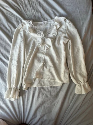 Vit blus med volang och spets. Från shein! - Söt vit blus med volangdetaljer längs ringningen och spetskant. Blusen har diskret prickstruktur i tyget och långa ärmar med breda manschetter. Perfekt för en romantisk och feminin look.