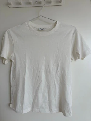 Klassisk vit t-shirt i bomull - En enkel och stilren vit t-shirt med rund hals och korta ärmar. Tillverkad i mjuk bomull som känns skön mot huden. Perfekt basplagg att matcha med allt i garderoben. Tidlös design utan tryck eller detaljer.