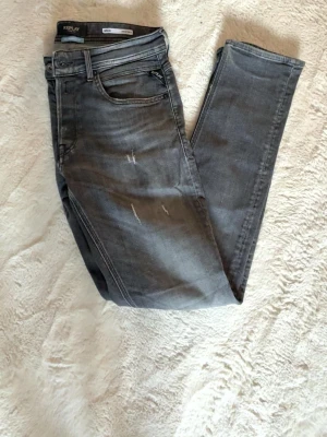Grå slim fit jeans från Replay - Snygga grå jeans från Replay i slim fit-modell. Jeansen har fem fickor, slitna detaljer framtill för en trendig look. Tillverkade i stretchigt material för extra komfort och passform.