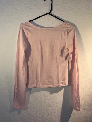 Ljusrosa långärmad topp - Säljer en enkel och stilren ljusrosa långärmad topp med låg ringning baktill. Toppen är gjord i mjuk bomull och har en normal passform som passar perfekt till jeans eller kjol.