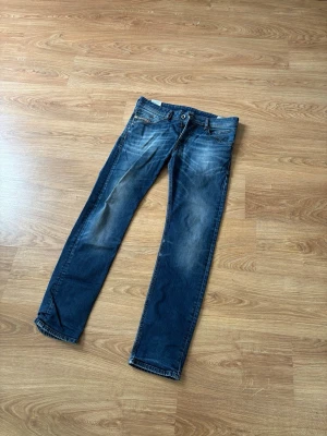 Diesel jeans - Säljer ett par klassiska blå jeans med raka ben och snygga slitningar framtill. Jeansen har fem fickor, knappgylf och kontrastsömmar. Materialet är denim i bomull och de har en avslappnad passform som funkar till det mesta.