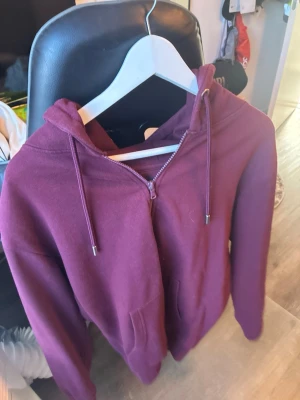 Vinröd hoodie från Sams Basic - Mysig vinröd hoodie från Sams Basic med dragkedja framtill, två fickor och justerbar huva med snören. Tillverkad i mjukt material som passar perfekt för chill dagar. Enkel och stilren design som funkar till det mesta.