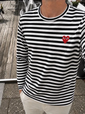 Comme des Garçons PLAY – Randig långärmad tshirt , M - Klassisk Comme des Garçons PLAY långärmad tröja i svart och vitt med det ikoniska röda hjärtat med ögon på bröstet. Tillverkad i 100% bomull och producerad i Japan. Stilren, tidlös och enkel att matcha med jeans eller chinos. Storlek M. Tröjan är i fint skick. En perfekt preppy/klassisk garderobsfavorit. Hör av er vid eventuella frågor och funderingar😊