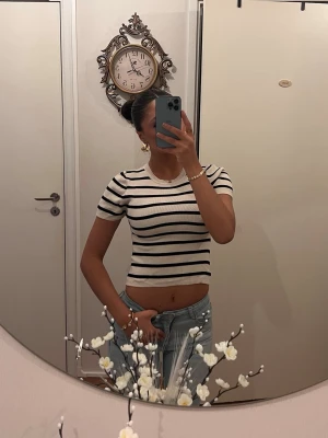Randig croppad topp i vitt och svart - Säljer en croppad topp med korta ärmar i vitt med svarta horisontella ränder. Toppen har en rund halsringning och sitter tight mot kroppen. Perfekt till jeans eller kjol för en trendig look.