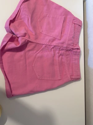 Rosa denimshorts med fickor - Snygga rosa shorts i denim med klassisk femficksmodell och uppvikta benslut. Shortsen har bälteshällor och dragkedja fram. Perfekta för sommaren och ger en färgklick till din outfit.