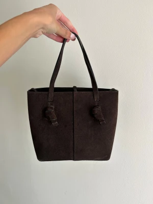 Mörkbrun mocka handväska - Otrolig väska från Massimo Dutti! Endast använd ett fåtal gånger, därav i nyskick!   Nypris 1500kr. Fläckar av vattenstänk förekommer på vänskan, syns bäst på sista bilden och därav priset. Annars som ny!  Långt band medkommer.   OBS! har bara möjlighet att sälja väskan under en kortare period