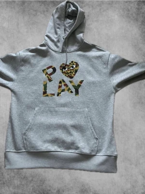 Grå hoodie med camo PLAY-tryck - Snygg grå hoodie med stor huva och känguruficka. På bröstet står det 'PLAY' i camomönster. Perfekt för dig som gillar casual och trendig stil. Mjuk och skön bomullsblandning. Om du har ytterligare frågor nå mig privat! 🤙🏻