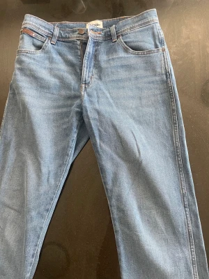 Ljusblå jeans från Wrangler - Säljer ett par klassiska ljusblå jeans från Wrangler med raka ben och fem fickor. 