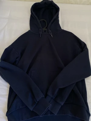 Mörkblå hoodie från Gina Tricot - En enkel och stilren mörkblå hoodie från Gina Tricot med huva och känguruficka framtill. Tillverkad i mjukt material och har ribbade muddar vid ärmslut och nederkant. Perfekt för en avslappnad look.