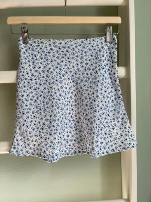 Kort A-linje kjol - Lågmidjad kortkjol med blåa blommor. Stl: 32 från hm i mycket bra skick.