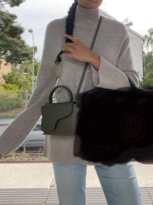 Beige polotröja med breda muddar - Mysig beige stickad polotröja med bred ribbad krage och muddar. Tröjan har en avslappnad passform och långa ärmar, perfekt för lager på lager. Materialet ser ut att vara mjukt och värmande, idealisk för kyligare dagar.