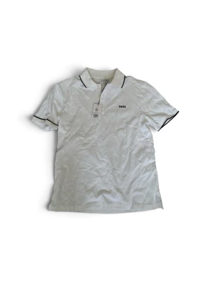 Vit pikétröja från BOSS - Vit pikétröja från BOSS med svart kant på krage och ärmslut. Klassisk design med korta ärmar och liten logga på bröstet. Perfekt för en clean och stilren look. Tröjan är aldrig använd och har kvar prislappen. (Den är dock lite skrynklig). Tröjan är i storlek 14 år och passar om man är ungefär mellan 165-175 (fråga gärna om mått ifall du är intresserad för jag är inte helt säker på storleken) pris kan även diskuteras!