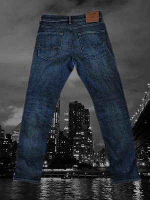 Mörkblå archive jeans - Snygga mörkblå jeans med klassisk femficksdesign och raka ben. Jeansen har en läderpatch bak i midjan och subtila slitningar för en avslappnad look. Passar perfekt till en streetwear-stil eller casual outfit.