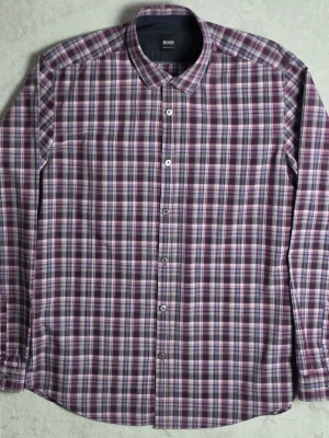 Hugo Boss Regular Fit skjorta rutig lila/blå L bomull - Snygg rutig skjorta från Hugo Boss i regular fit-passform. Klassisk färgkombination i lila, blått och vitt som passar både vardag och mer uppklätt.  • Storlek L • Regular Fit  Skick • Bra använt skick • Inga större anmärkningar  Mått • Bröstbredd: ca 55 cm • Plagglängd: ca 76 cm • Axelbredd: ca 46 cm • Ärmlängd: ca 65 cm  Material • 100% bomull