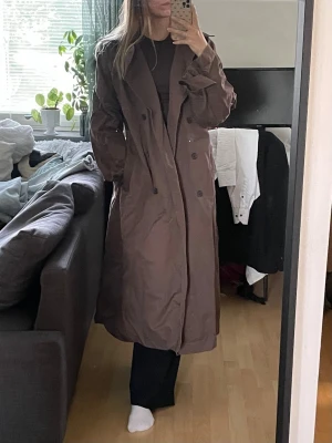 Mörkbrun lång trenchcoat - Mörkbrun lång trenchcoat från Weekday i storlek s. Skulle säga att den är en stor s, så passar nog främst om man är en större s eller brukar ha m. Jag är 173 och den är bra i längd både i ärmar och ner över halva vaderna. I väldigt fint skick!