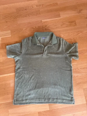 Grön pikétopp i frotté - En grön pikétopp i mjuk frotté med klassisk krage och knappar framtill. Kortärmad modell med relaxed fit och enkel design som ger en chill vibe.