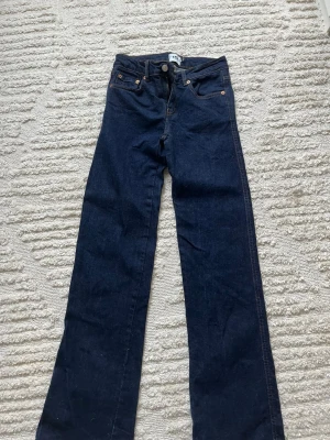 Mörkblå raka jeans från 770 - Säljer ett par mörkblå jeans med boot cut och klassisk femficksdesign. Jeansen har kontrastsömmar och metallknappar samt en läderpatch bak i midjan. Perfekta för dig som gillar en tidlös och enkel look.