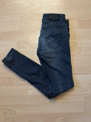 Nudie Jeans - Mörkgrå - Snygga mörkblå Nudie Jeans med klassisk denimtvätt. Stilren modell med snygga detaljer och naturliga slitningar. Bra begagnat skick. 📏 Storlek: W26 L32 👖 Färg: Mörkblå 📦 Skickas snabbt