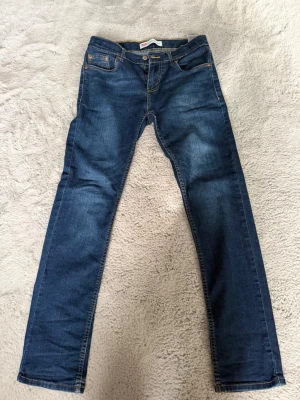Mörkblå raka jeans från Levi's slim taper  - Snygga mörkblå jeans från Levi's med klassisk femficksmodell och raka ben. Jeansen har kontrastsömmar och en liten röd Levi's-tag på bakfickan. Tillverkade i slitstarkt denimtyg som ger en tidlös look.