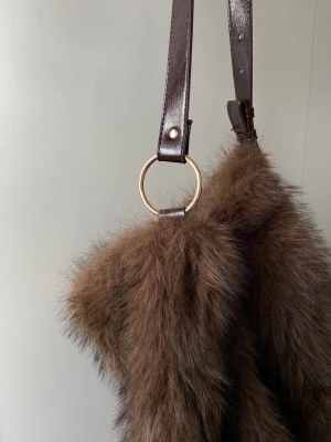 Stradivarius väska i fuskpäls - Superfin fuskpäls väska från Stradivarius i nyskick. Den har en brun rem som kan justeras till axelrem eller crossover och gulddetaljer🤍Väskan är lagom stor och får plats med dator mm.  Nypris 300kr