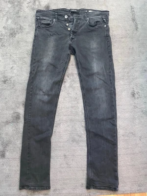 Replay slim fit - Säljer ett par svarta replay slim fit jeans med knappgylf och fem fickor. Jeansen har diskreta slitningar och vita sömmar som kontrast. Passar perfekt till en avslappnad och trendig stil. Materialet är klassisk denim med lite stretch. Som ni även ser på bild 1 så är det två hål som är ihopsydda på vänster ben.