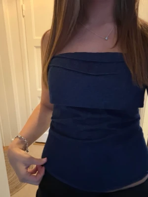Mörkblå bandeau tubtopp - Säljer en mörkblå bandeau tubtopp med snygga lagerdetaljer framtill. Toppen är tight och axelbandslös, perfekt för varma dagar eller när du vill ha en clean look. Materialet känns mjukt och stretchigt, vilket gör den bekväm att bära.