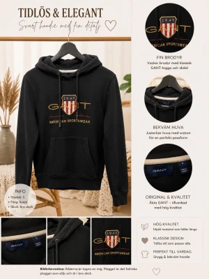 Svart hoodie med GANT-brodyr - Svart hoodie från GANT med broderad logga och sköld i guld, rött och vitt på bröstet. Klassisk känguruficka framtill, justerbar huva med snören och ribbade muddar. Tillverkad i mjukt material för en bekväm känsla.