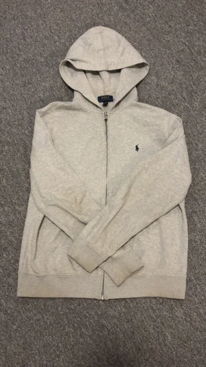 Ralph Lauren - Äkta Ralph Lauren zip hoodie i stilren grå färg. Riktigt bra skick. Nypris ligger runt 2000 kr. Har en riktigt lite fläck på armen skriv om ni vill ha bild på fläcken! Pris kan diskuteras!