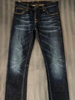 Mörkblå Slim jeans med slitningar - Säljer ett par mörkblå jeans med  snygga slitningar framtill och baktill. Jeansen har klassisk femficksdesign och kontrastsömmar. Materialet är denim i bomull och de har en cool, tvättad look.