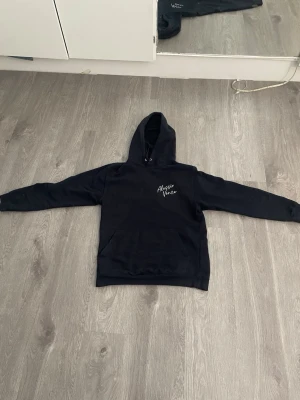 Alessio vence hoodie - Säljer en svart hoodie med huva och magficka. På bröstet finns ett vitt tryck med texten 'Alesso Voca'. Hoodien har klassisk passform och ribbade muddar vid ärmar och nederkant. Perfekt för en avslappnad och stilren look.